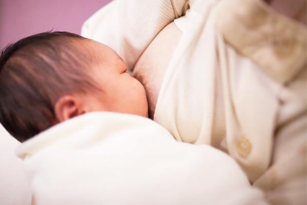 Un bebé recién nacido amamantando, envuelto en una manta blanca