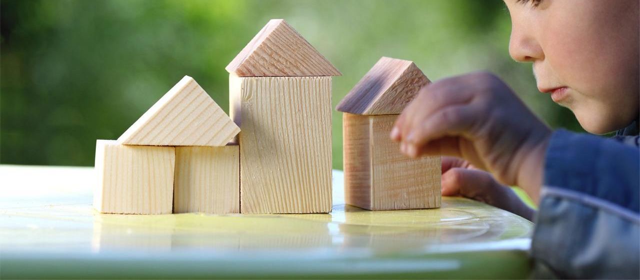 Un niño concentrado construyendo casitas con bloques de madera sobre una mesa, al aire libre